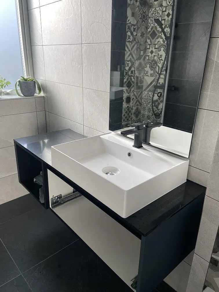 Tvättställsbänk i svart Silestone Eternal Noir, polerad, med ett vitt keramikfat och svart blandare i ett badrum under montering i Stora höga.