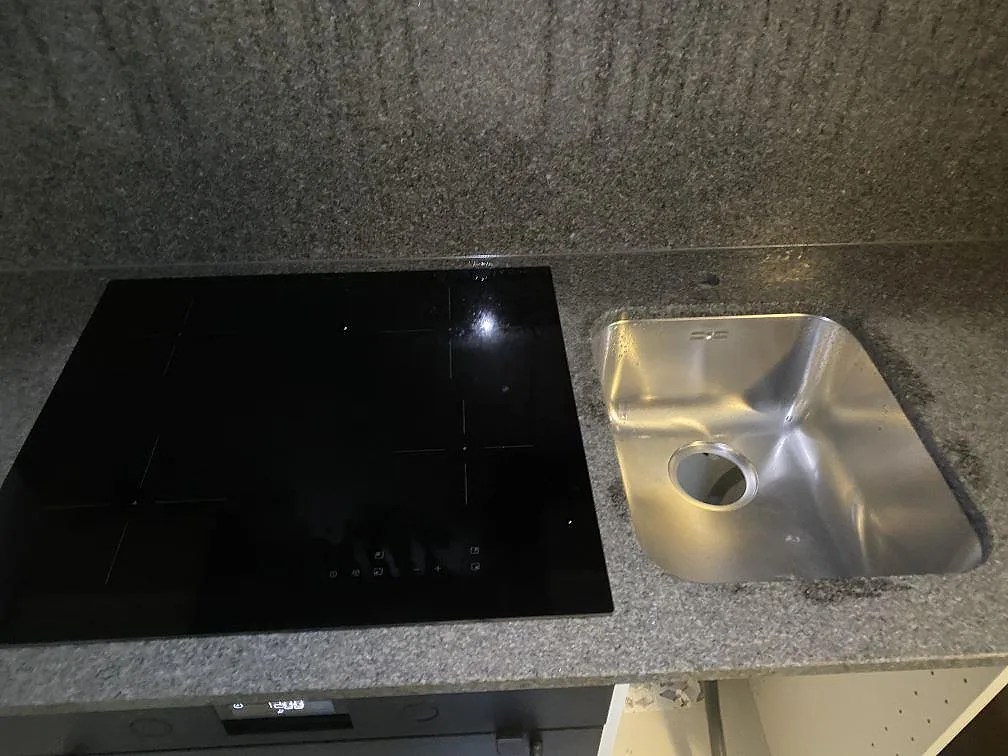 Köksbänkskiva i grå Silestone Eternal Serena med svart induktionshäll och underlimmad rostfri diskho i ett kök i Malmö.