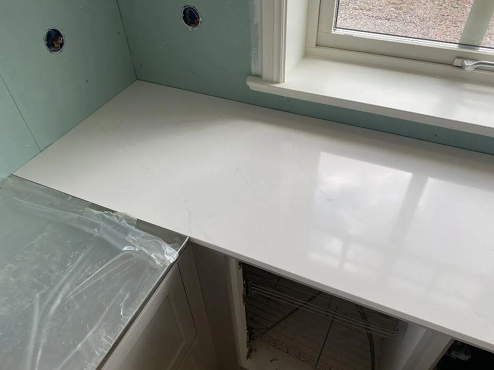 Köksö i Silestone Eternal Statuario med uppvikt hörn och diskret grå ådring i ett kök under montering i Åryd.