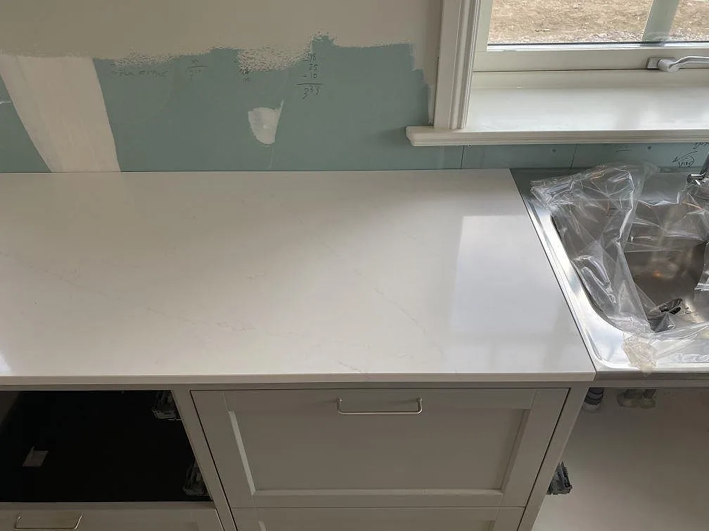 Bänkskiva i vit Silestone Eternal Statuario, polerad, med underlimmad rostfri diskho och diskret grå ådring i ett kök i Åryd.