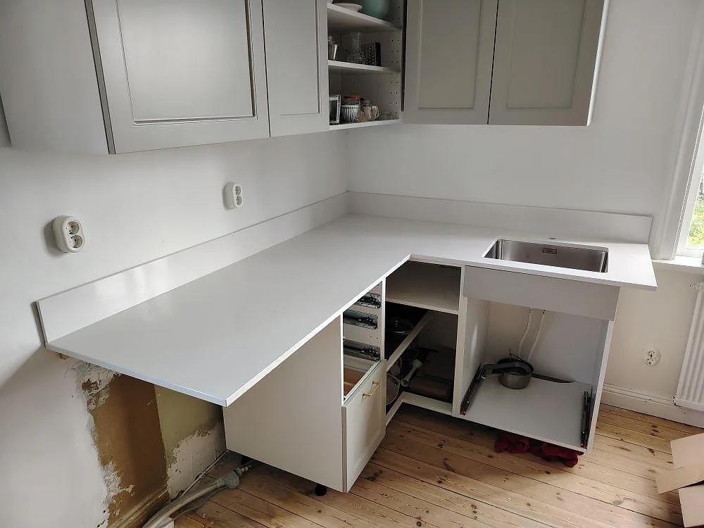 L-format köksbänkskiva i vit Silestone Eternal Statuario, polerad, med rostfri diskho och låg stänkkant i ett kök i Älvsjö.