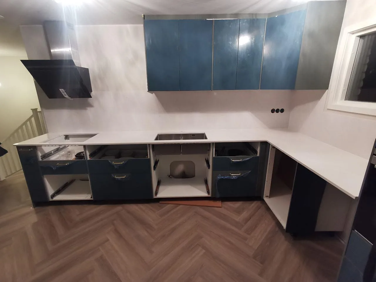 Köksbänkskiva i vit Silestone Eternal Statuario, polerad, i ett L-format kök i Borås med blåa blanka luckor, fiskbensgolv och underlimmad rostfri diskho, fotograferat under montering.