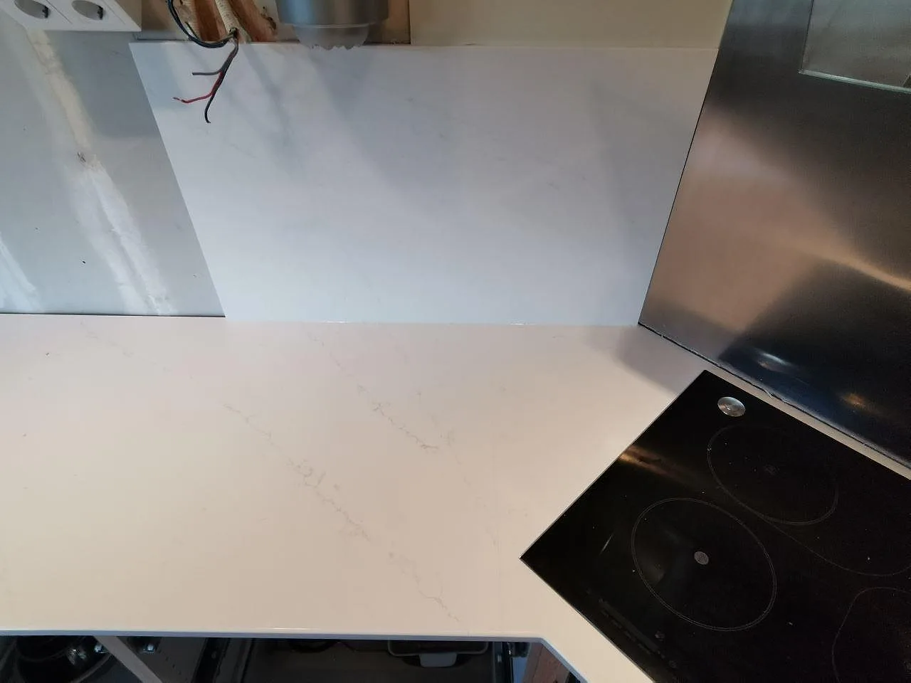 Köksbänkskiva i vit Silestone Eternal Statuario mot rostfri vägg med induktionshäll i ett kök i Borås under montering.