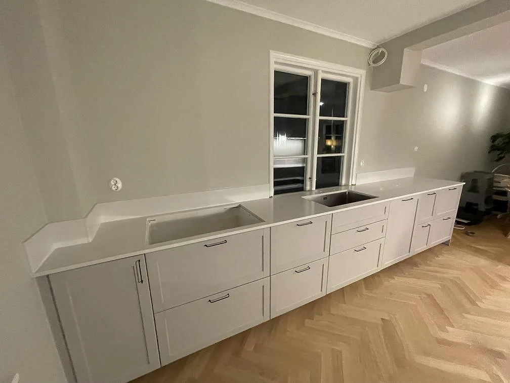 Lång köksbänkskiva i vit Silestone Eternal Statuario, polerad kvartskomposit, med två diskhoar och lågt stänkskydd i ett kök i Bromma.