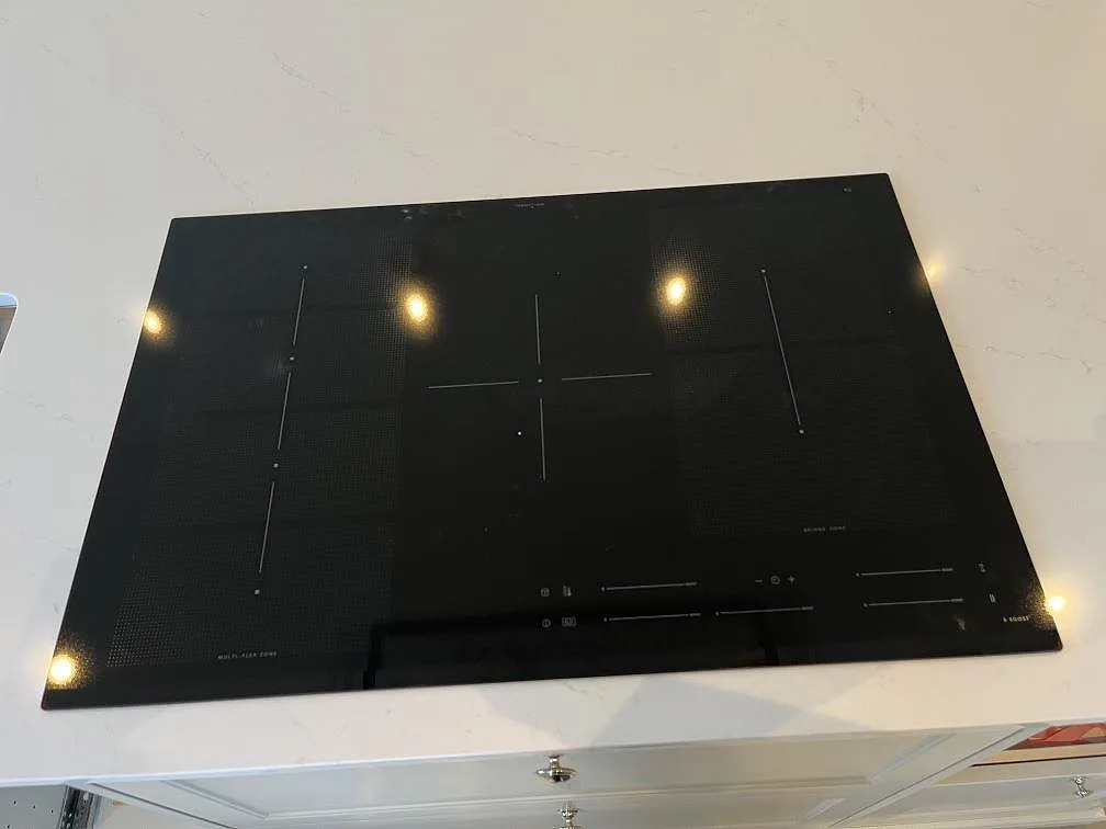 Svart induktionshäll infälld i en polerad vit Silestone Eternal Statuario köksbänkskiva med grå ådring i Färjestaden.