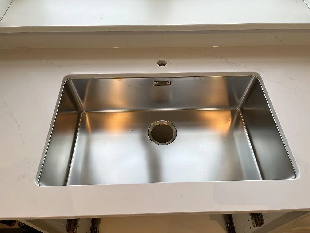 Stor underlimmad rostfri diskho i en polerad Silestone Eternal Statuario bänkskiva, med separat blandarhål borrat i stenen, i ett kök i Färjestaden.