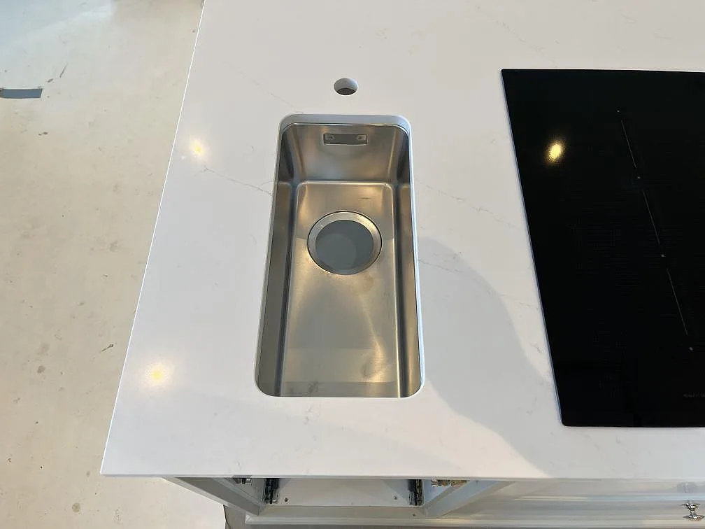 Mindre underlimmad rostfri extradiskho i vit Silestone Eternal Statuario bredvid en svart induktionshäll i ett kök i Färjestaden.