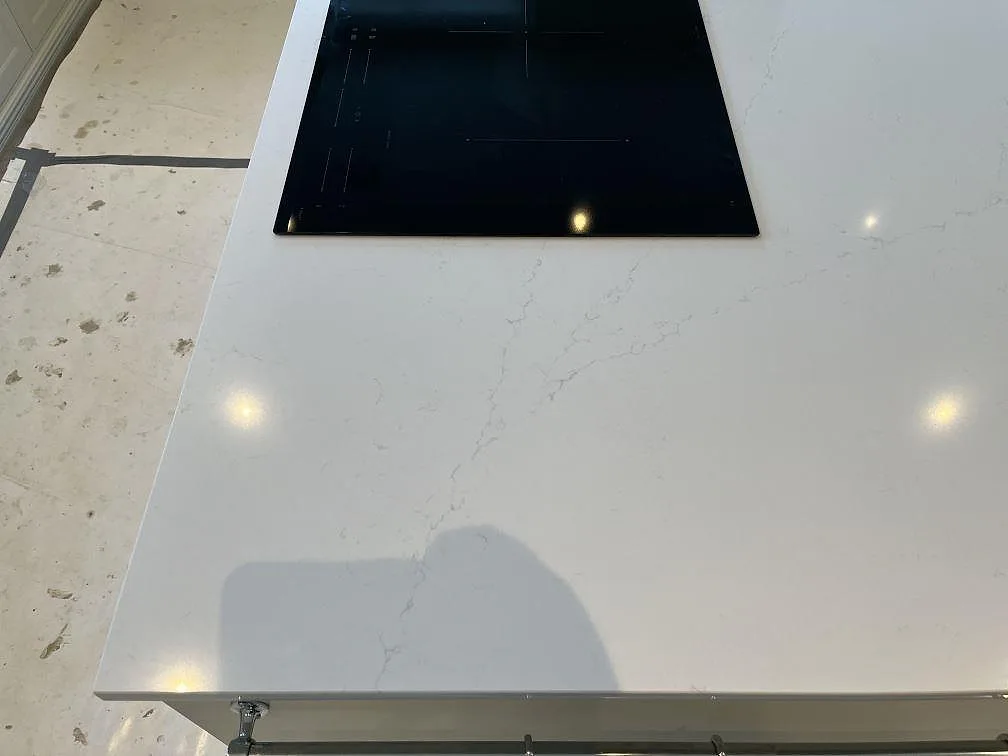 Bred köksbänk i polerad Silestone Eternal Statuario med infälld svart induktionshäll och tydlig grå ådring i ett kök i Färjestaden.