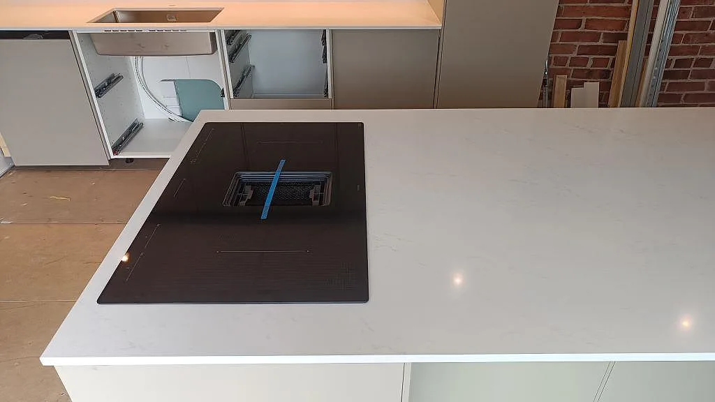 Polerad köksbänkskiva i Silestone Eternal Statuario med svart häll infälld i den ljusa kvartskompositen i Halmstad.