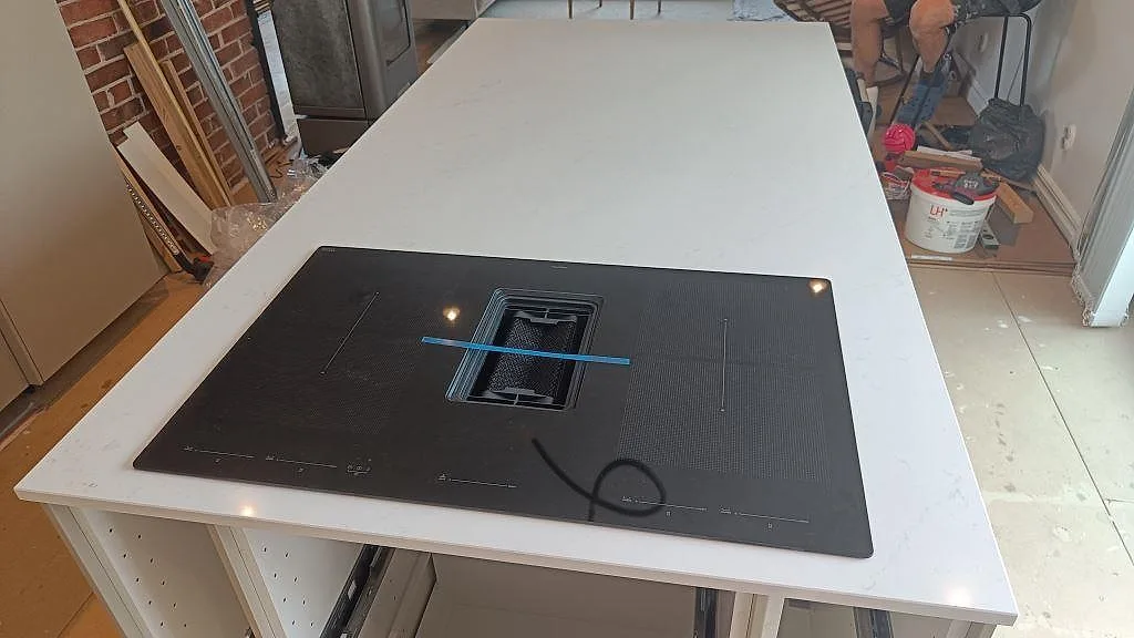 Närbild av köksö i polerad Silestone Eternal Statuario med svart häll och ljus ådring under montering i Halmstad.