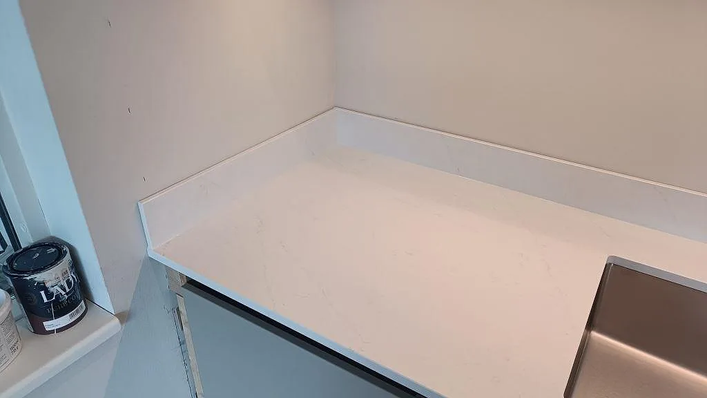 Köksbänkskiva i polerad Silestone Eternal Statuario med uppvikt stänkkant och diskho vid vägg i Halmstad.