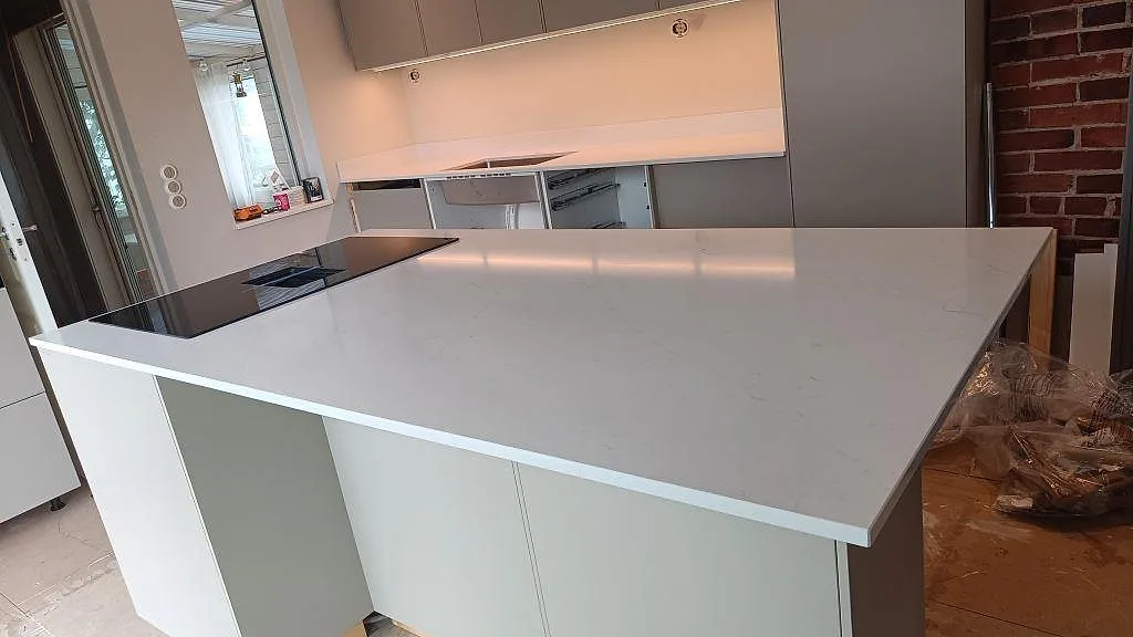 Köksbänkskiva i vit Silestone Eternal Statuario, polerad, på en köksö med svart häll och exponerad tegelvägg i Halmstad.