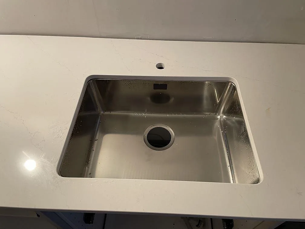 Underlimmad rostfri diskho i polerad Silestone Eternal Statuario med synligt blandarhål och mjuk grå ådring i ett kök i Kävlinge.