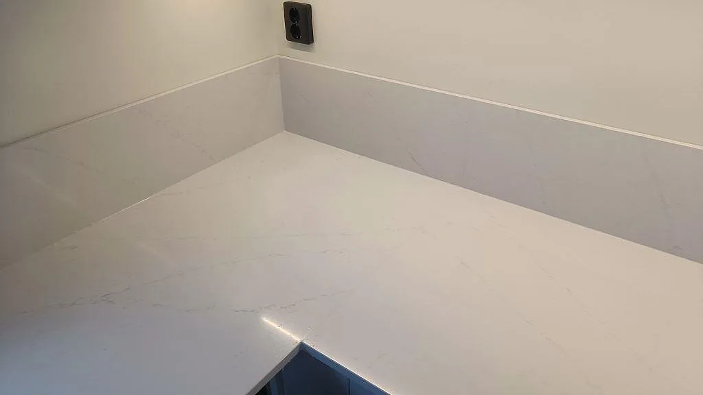 Hörnparti av polerad Silestone Eternal Statuario med uppvikt stänkkant och diskret grå ådring i ett kök i Karlshamn.