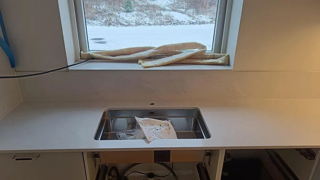 Underlimmad rostfri diskho i vit Silestone Eternal Statuario under ett fönster med snöutsikt i ett kök i Karlshamn.