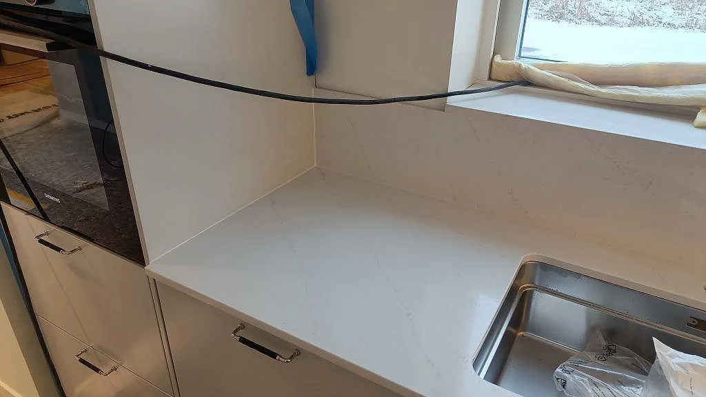 Bänkskiva i vit Silestone Eternal Statuario med underlimmad rostfri diskho intill fönstret i ett kök i Karlshamn.
