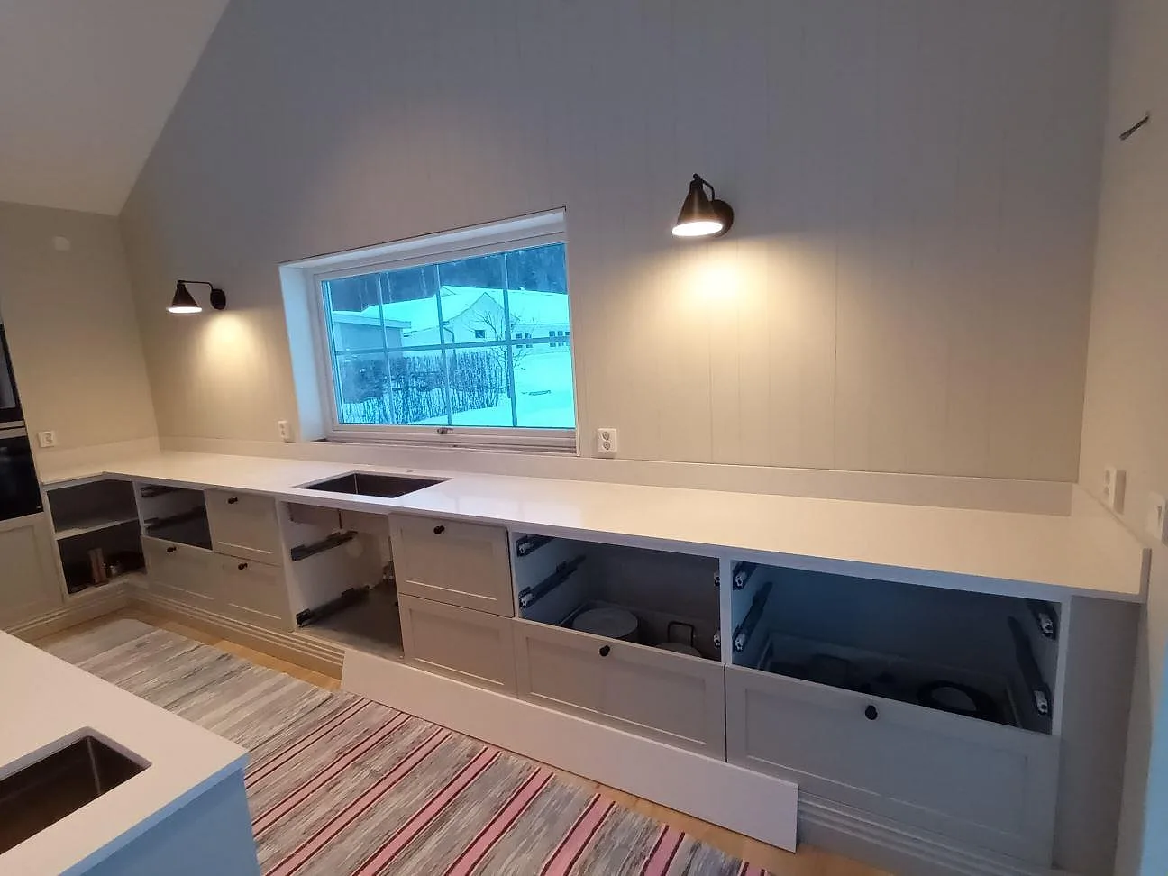 Bänkrad i vit Silestone Eternal Statuario under fönstret med diskhourtag, polerad yta, i ett kök i Leksand.