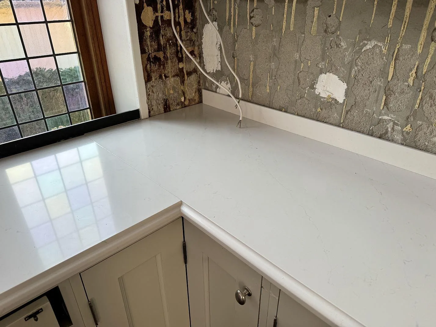 Hörnparti med polerad Silestone Eternal Statuario bänkskiva, låg stänkkant och ljus komposityta i kök i Limhamn.