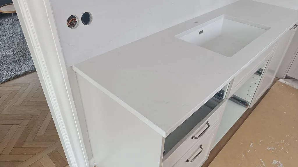 Köksbänkskiva i vit Silestone Eternal Statuario, polerad, med diskho och ljus ådring i ett kök under montering i Limhamn.