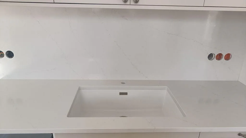 Polerad Silestone Eternal Statuario som bänkskiva och stänkskydd vid diskho i ett vitt kök i Limhamn.