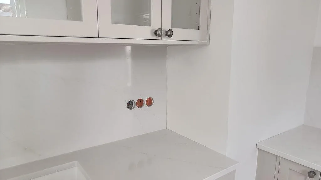 Köksbänkskiva och väggskiva i polerad Silestone Eternal Statuario runt diskhozonen i ett ljust kök i Limhamn.