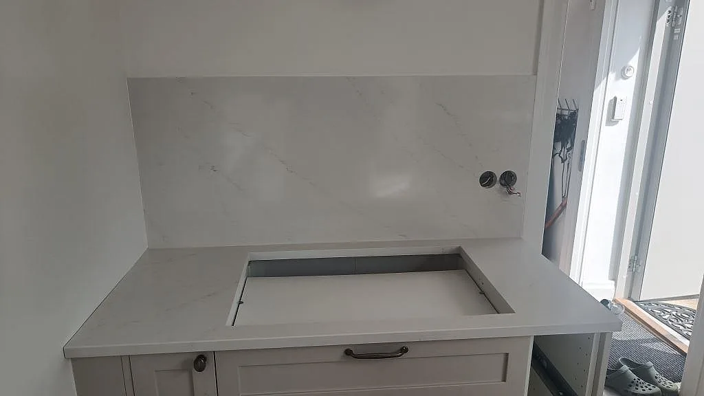 Polerad Silestone Eternal Statuario med stor hällöppning och väggskiva i en köksnisch under montering i Limhamn.
