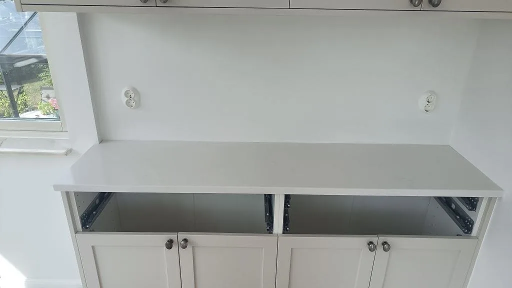 Lång bänkyta i vit Silestone Eternal Statuario, polerad, intill fönster och vita köksstommar i Limhamn.