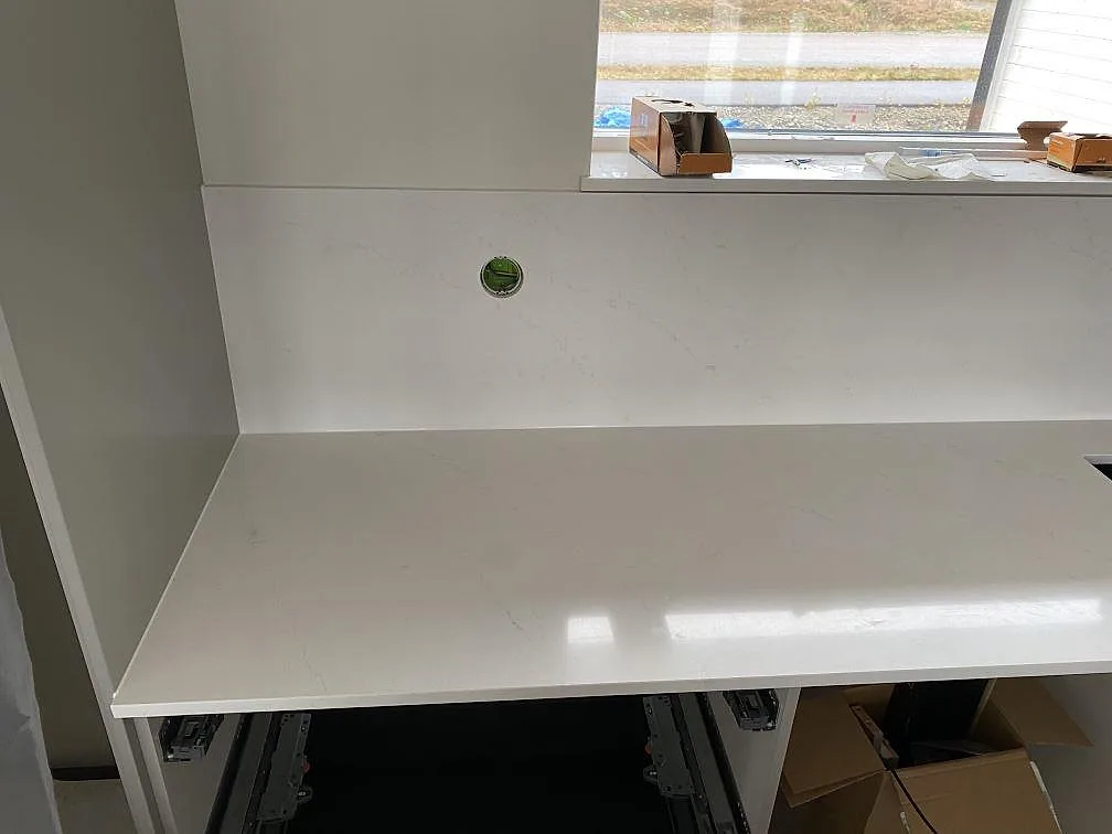 Lång köksbänkskiva i Silestone Eternal Statuario med uppvikt stänkskydd och öppna vita köksstommar under montering i Ljungby.