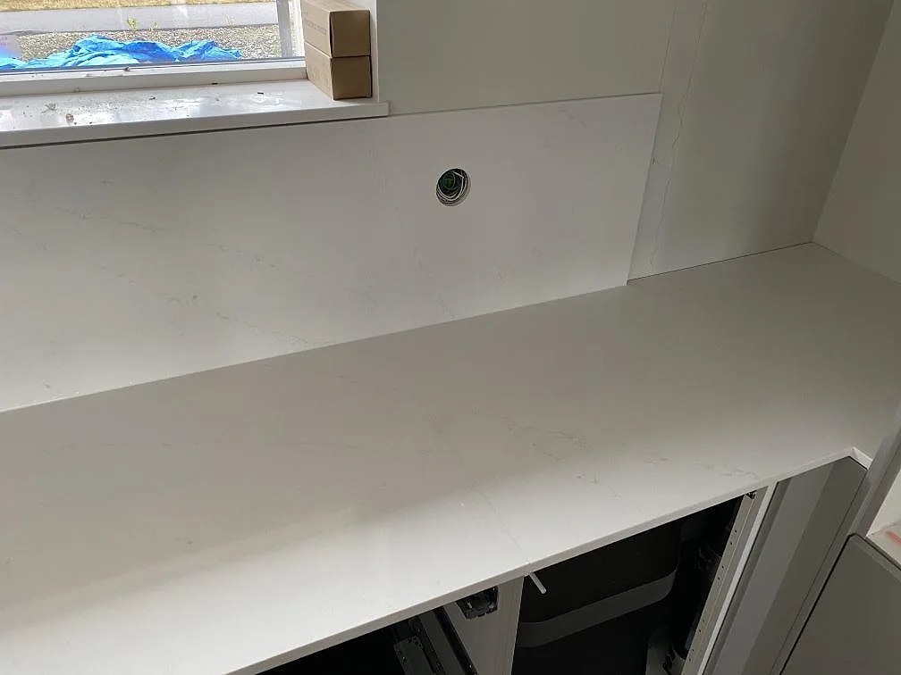 Hörn av köksbänkskiva i vit polerad Silestone Eternal Statuario med matchande stänkskydd och eluttag i Ljungby.
