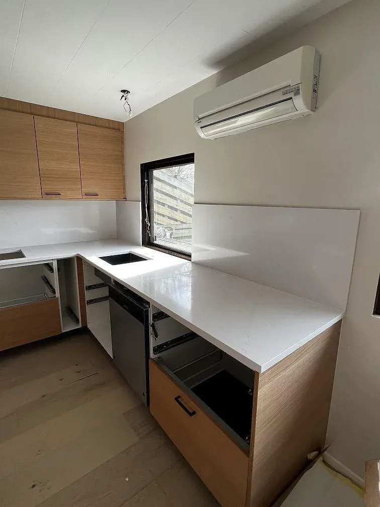 Kringgående köksbänk i polerad vit Silestone Eternal Statuario med nedsänkt svart diskho under fönstret i ett kök i Löddeköpinge.