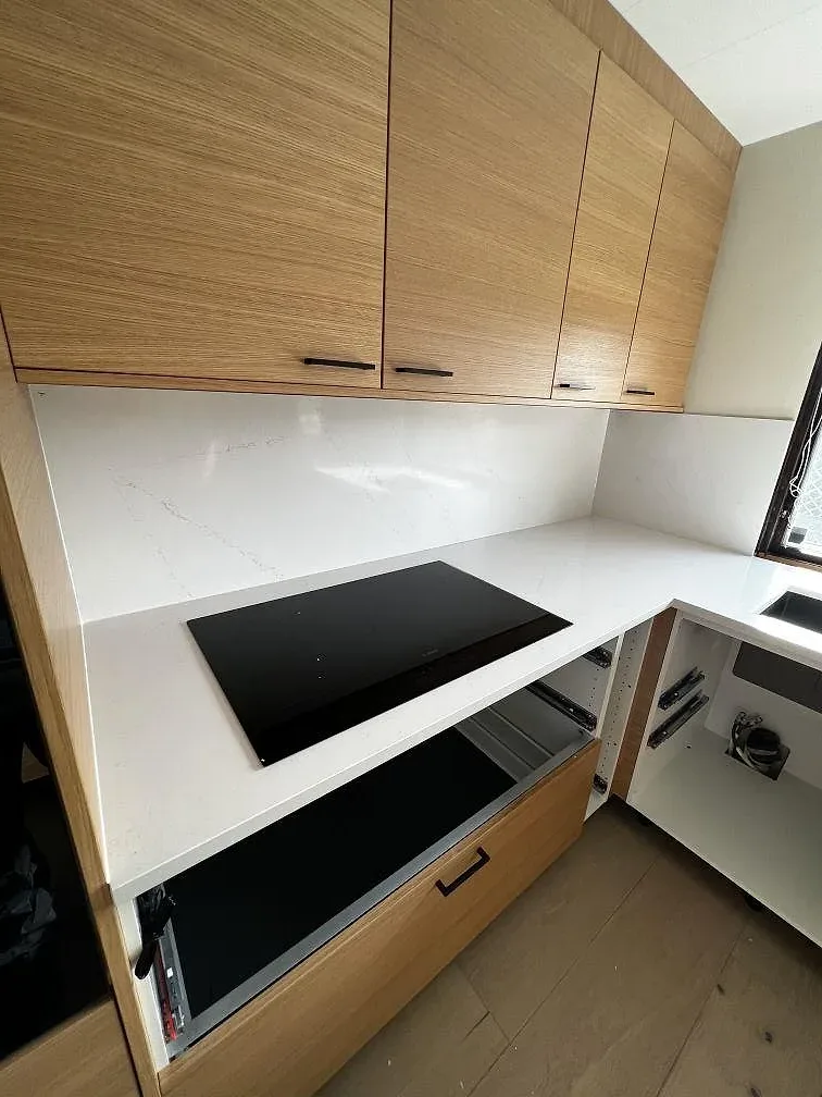 Svart induktionshäll infälld i polerad vit Silestone Eternal Statuario bänkskiva längs en köksbänk med ekluckor i Löddeköpinge.