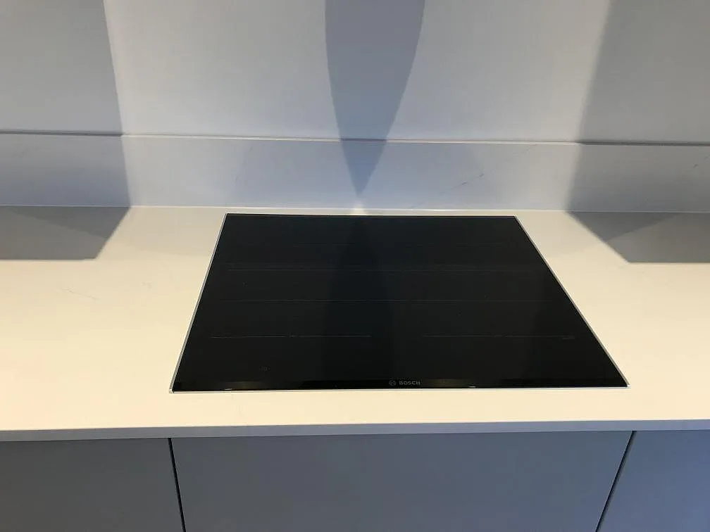 Köksbänkskiva i vit Silestone Eternal Statuario med en infälld Bosch induktionshäll och uppvikt stänkkant i ett kök i Lomma.