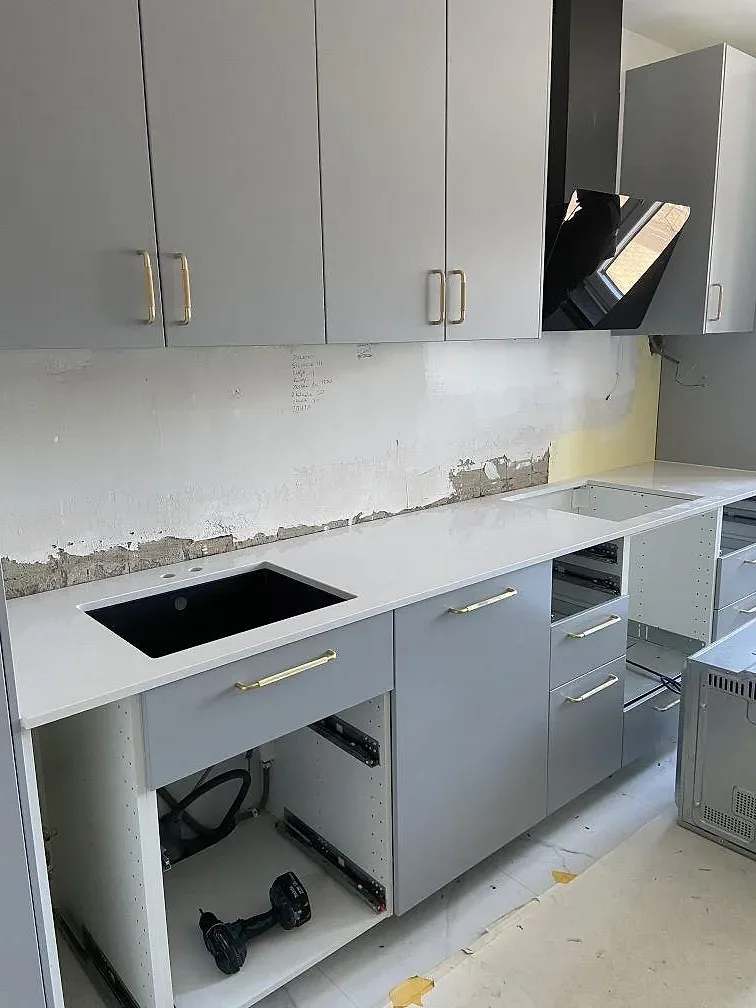 Köksbänkskiva i vit Silestone Eternal Statuario med svart underlimmad diskho och grå stommar under montering i ett kök i Malmö.
