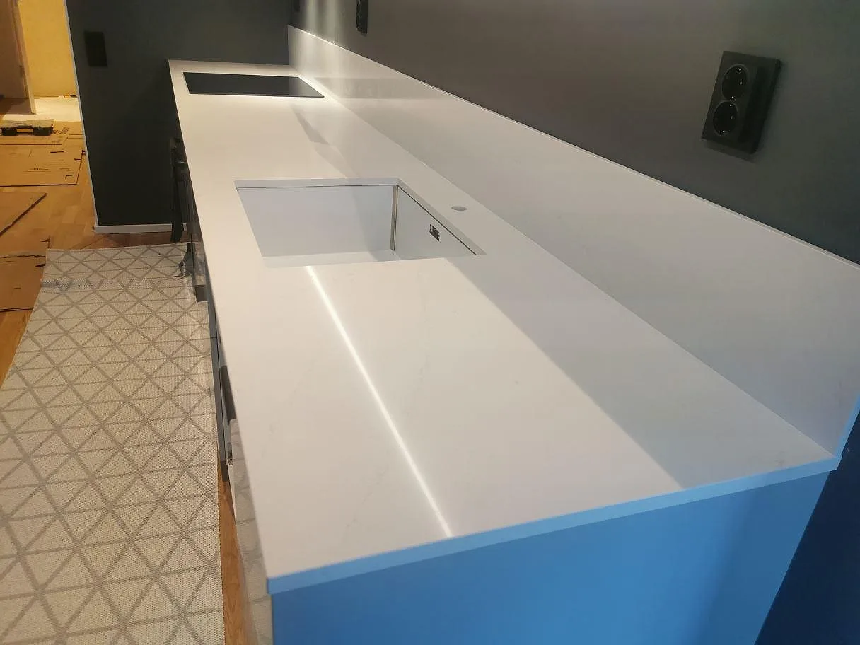 Köksbänkskiva i vit Silestone Eternal Statuario, polerad, med grå ådring och urtag för underlimmad diskho och induktionshäll i ett kök under montering i Nacka.