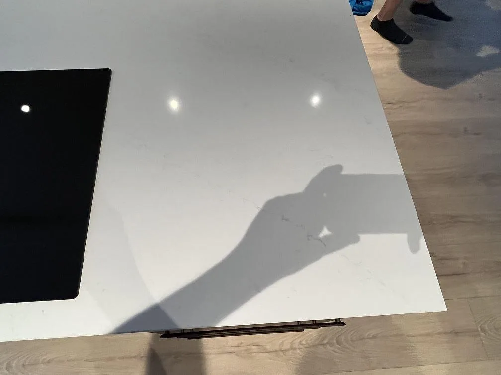 Detalj av polerad Silestone Eternal Statuario komposit på köksö med svart induktionshäll och speglingar i Rönninge.