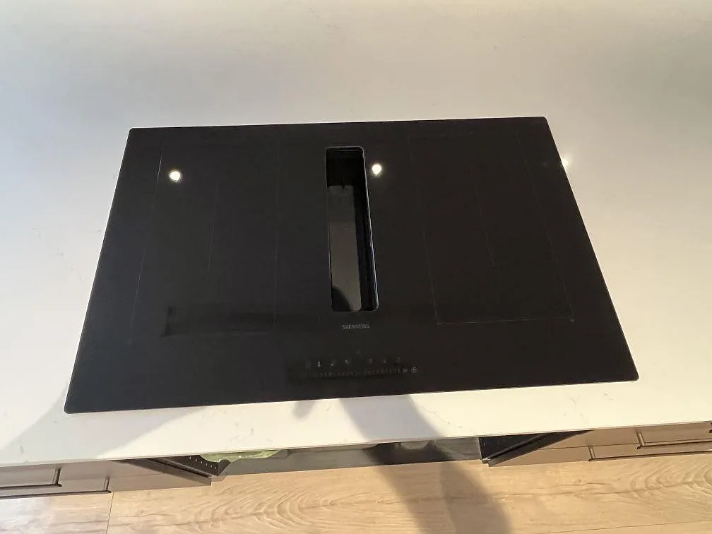 Närbild på svart induktionshäll i en polerad Silestone Eternal Statuario köksö med ljus ådring i Rönninge.