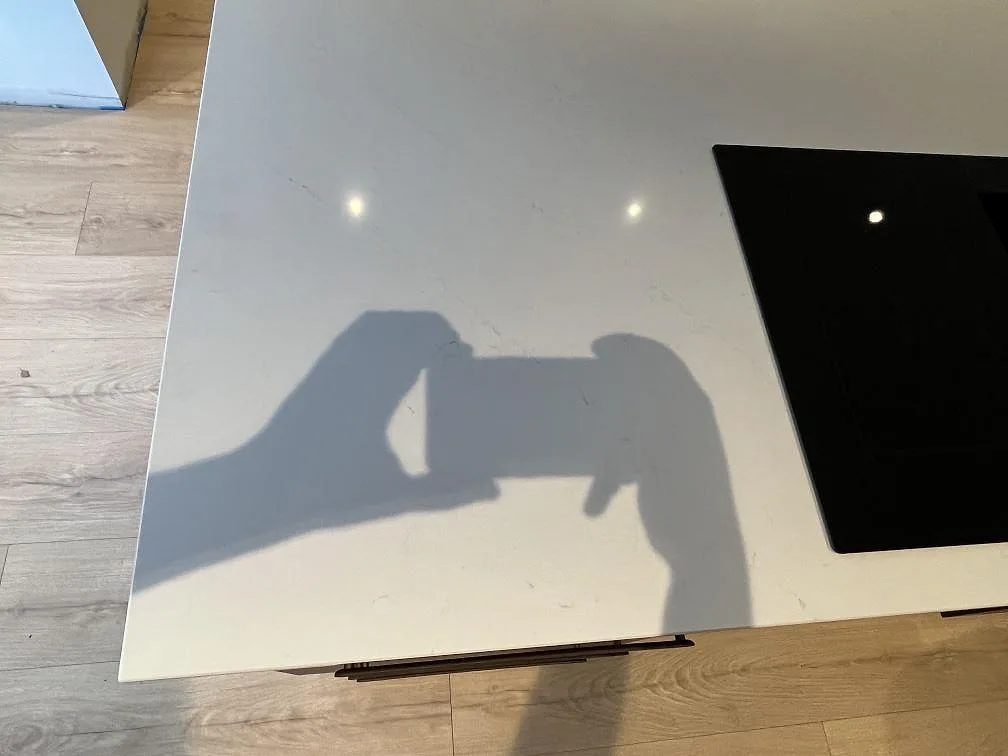 Polerad vit Silestone Eternal Statuario på köksö med grå ådring och svart häll vid kanten i Rönninge.