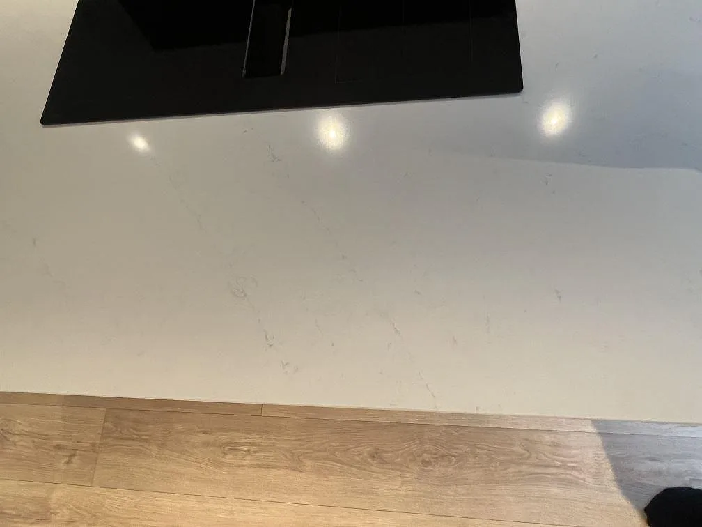 Närbild av polerad Silestone Eternal Statuario komposit framför den svarta induktionshällen på köksön i Rönninge.