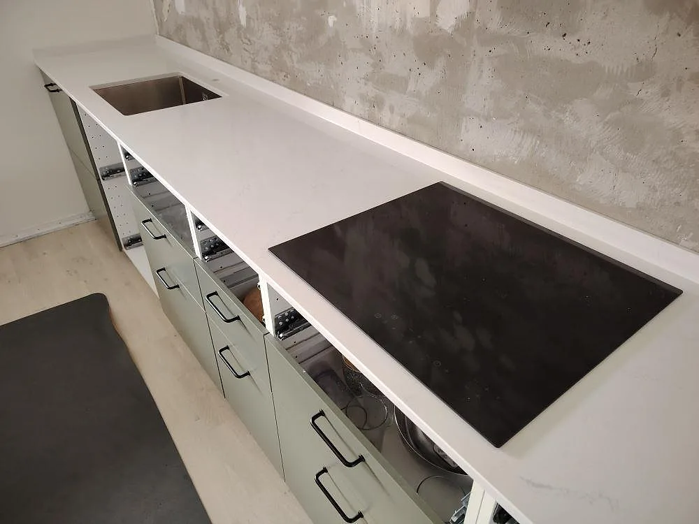 Närbild av polerad Silestone Eternal Statuario som köksbänkskiva med häll, diskho och mjuk grå ådring under montering i Stockholm.