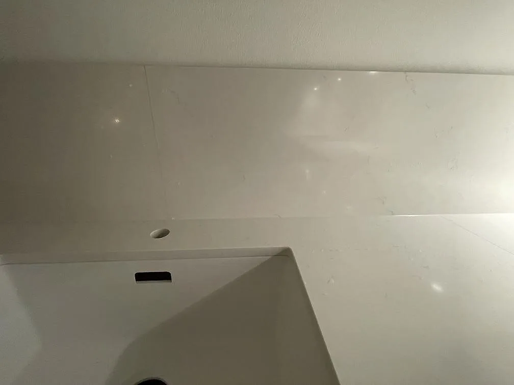Närbild på uppvikt stänkkant och diskhokant i polerad vit Silestone Eternal Statuario kvartskomposit i ett kök i Stockholm.