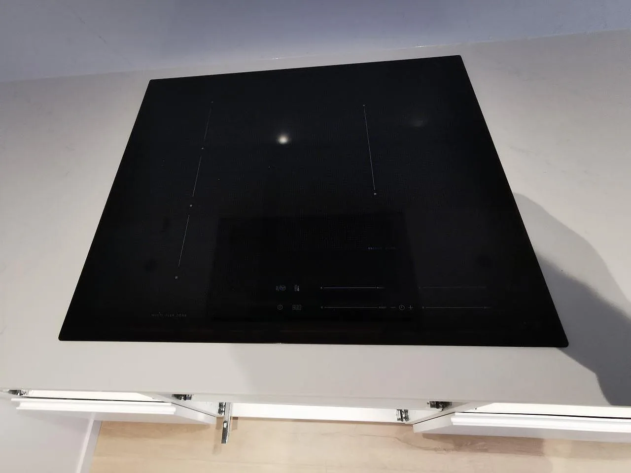 Övermonterad svart induktionshäll infälld i polerad vit Silestone Eternal Statuario-bänkskiva i ett kök i Svedala.