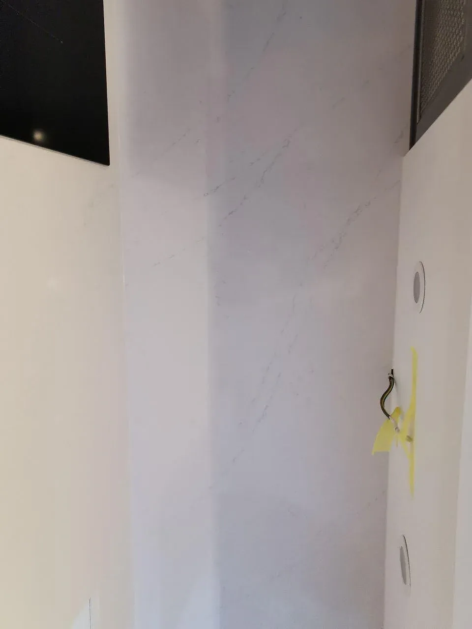 Stänkskydd i polerad vit Silestone Eternal Statuario med diskret grå ådring bakom köksfläkten i Svedala.