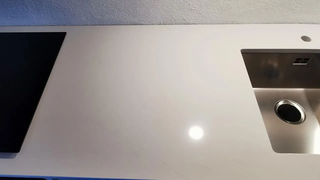 Köksbänkskiva i vit Silestone Eternal Statuario, polerad, med underlimmad rostfri diskho och svart induktionshäll ovanpå stenen i ett kök i Trelleborg.
