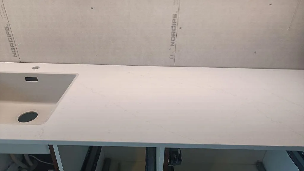 Lång köksbänkskiva i polerad Silestone Eternal Statuario med diskho till vänster och öppen stomme i Varberg.