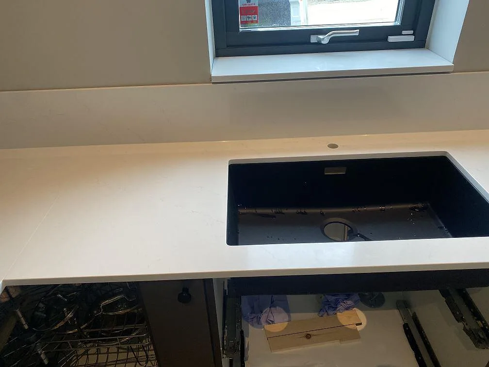 Polerad bänkskiva i Silestone Eternal Statuario med underlimmad svart kompositdiskho i ett kök i Vellinge.