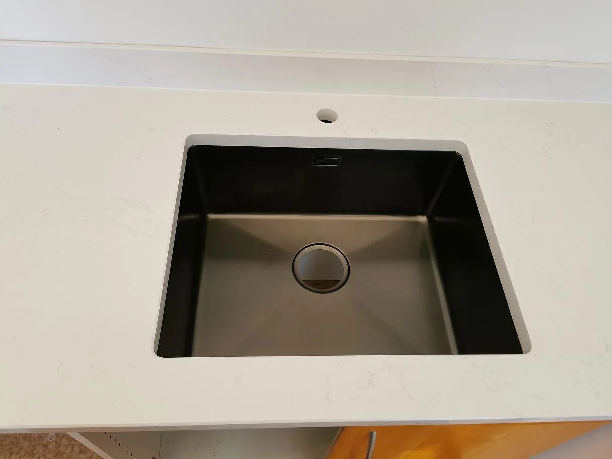Underlimmad diskho i en polerad köksbänkskiva av vit Silestone Eternal Statuario i ett kök i Ystad.