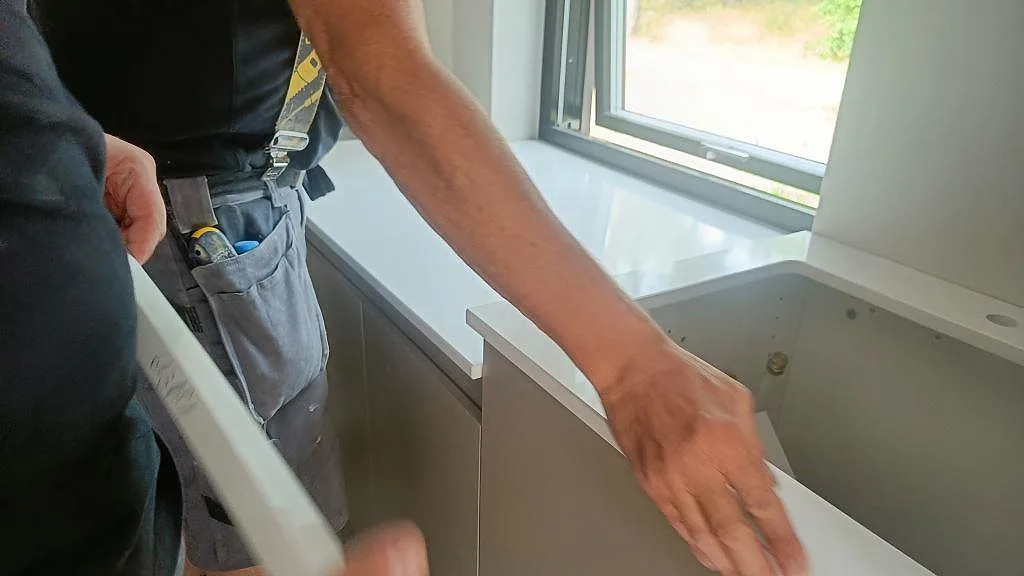Montering av Silestone Eternal Statuario i kök i Ystad, en stänkskiva i vit kvartskomposit hanteras vid bänken.