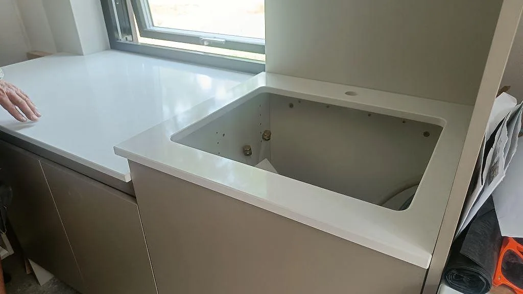 Köksbänkskiva i vit Silestone Eternal Statuario, polerad, med urtag för underlimmad diskho längs fönstervägg i ett kök i Ystad.