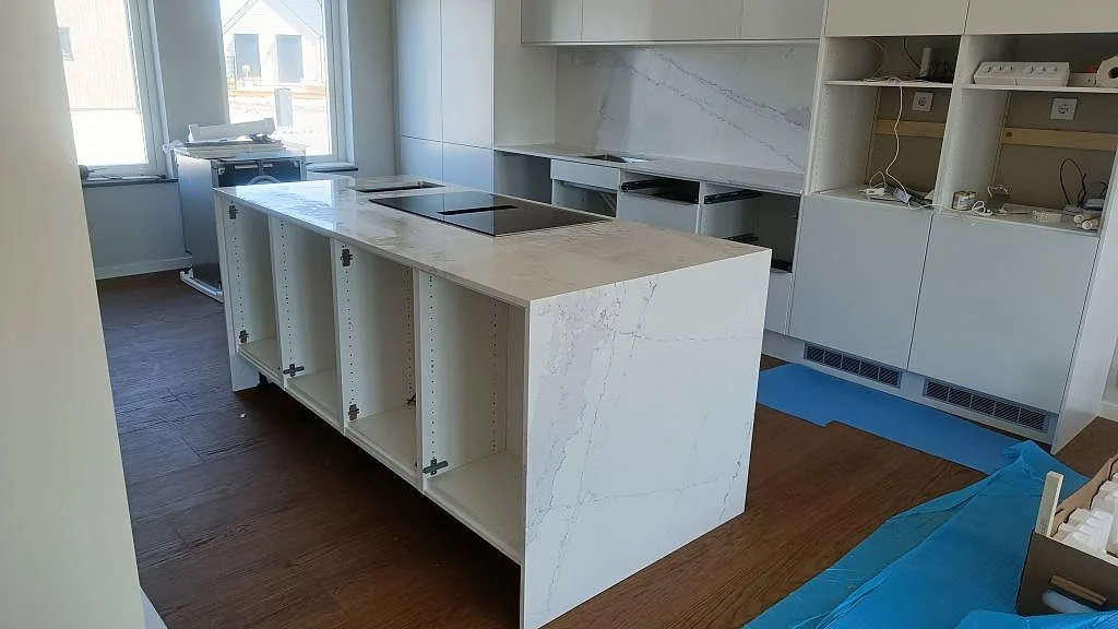 Köksbänkskiva och köksö i vit Silestone Ethereal Dusk, polerad komposit, med vattenfallssida och svart induktionshäll i ett kök i Halmstad.