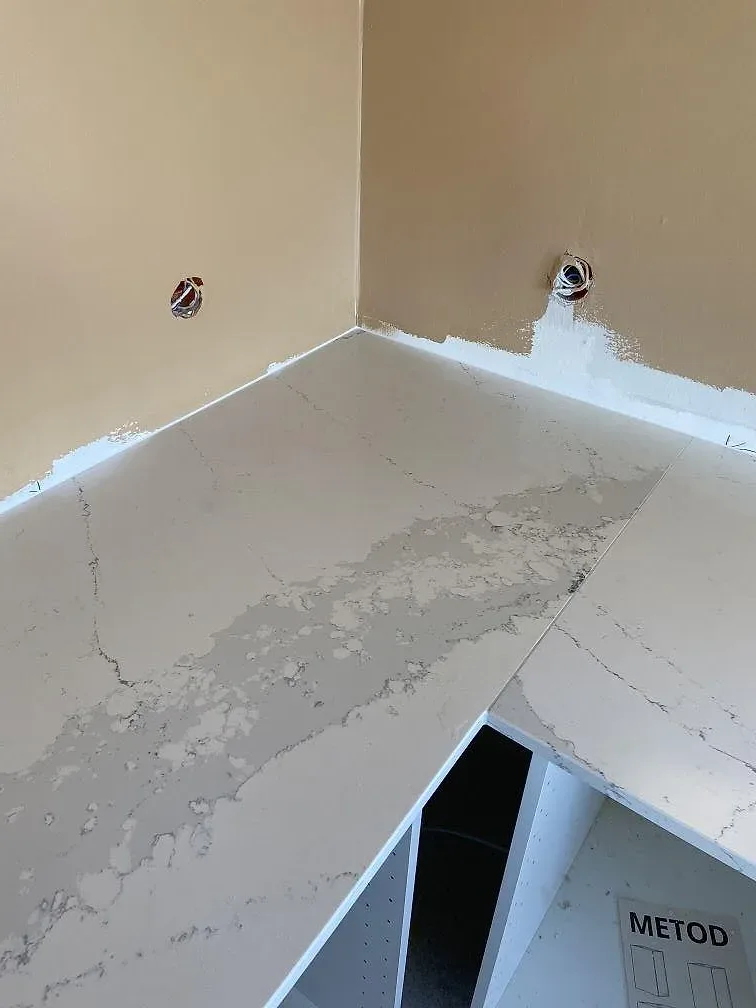 Vit Silestone Ethereal Dusk bänkskiva sedd uppifrån i en hörnsektion med urtag för eluttag, monterad mot oputsad vägg i ett kök i Oxie.